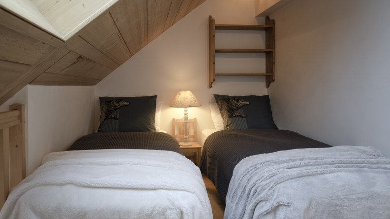 Chambre avec deux lits simples, plafond mansard avec un velux, rangement  la tte du lit droit, se situe sur une mezzanine