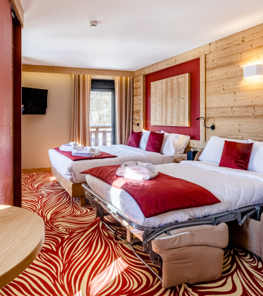 Chambre avec deux lits double et couvre lit rouge. Moquette rouge et beige et coin caf.