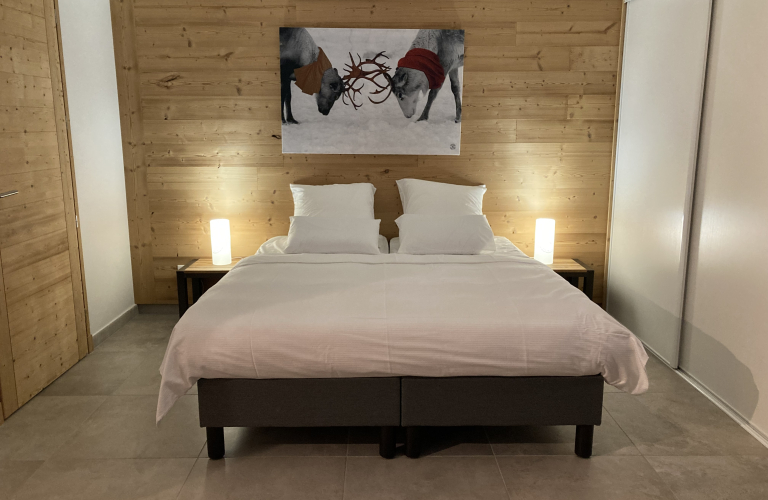 Chambre avec un lit double au milieu, une table de nuit sur les deux ct du lit, un placard sur le mur droit et une porte sur le mur gauche, un tableau avec deux cerfs sur le mur  la tte de lit.