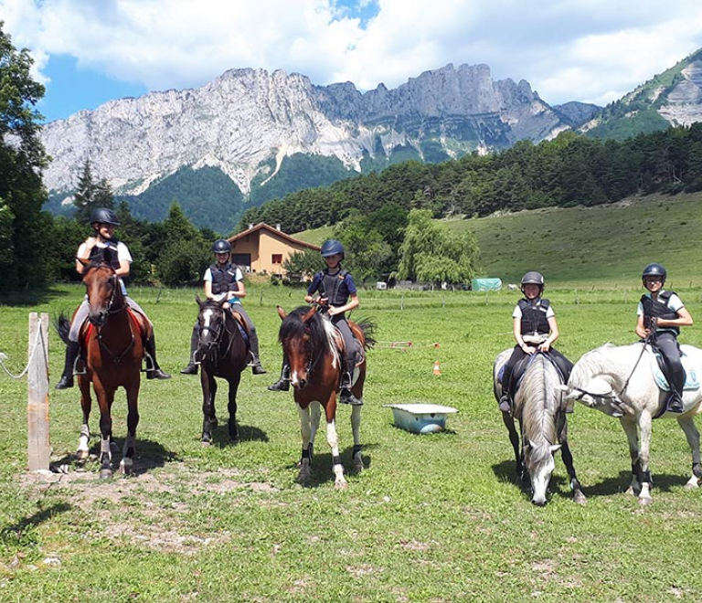 Un groupe d'adolescents  cheval se promnent dans une nature verdoyante, une montagne domine l'horizon contre le ciel bleu